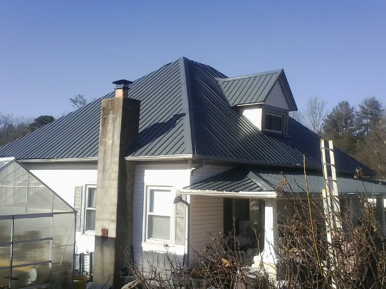 Dark blue standing seam metal roof on a white farmhouse with dormer — Slate & Tile Roof Repair by Roofing Brothers in Farmersville