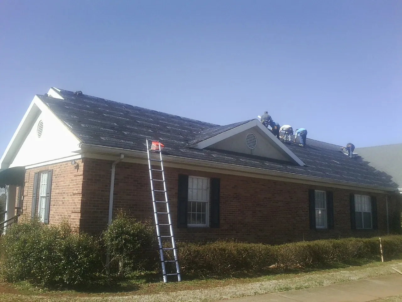 Crew tearing shingles off a brick ranch roof with a ladder set — Emergency Roof Repair work by our crew in Farmersville