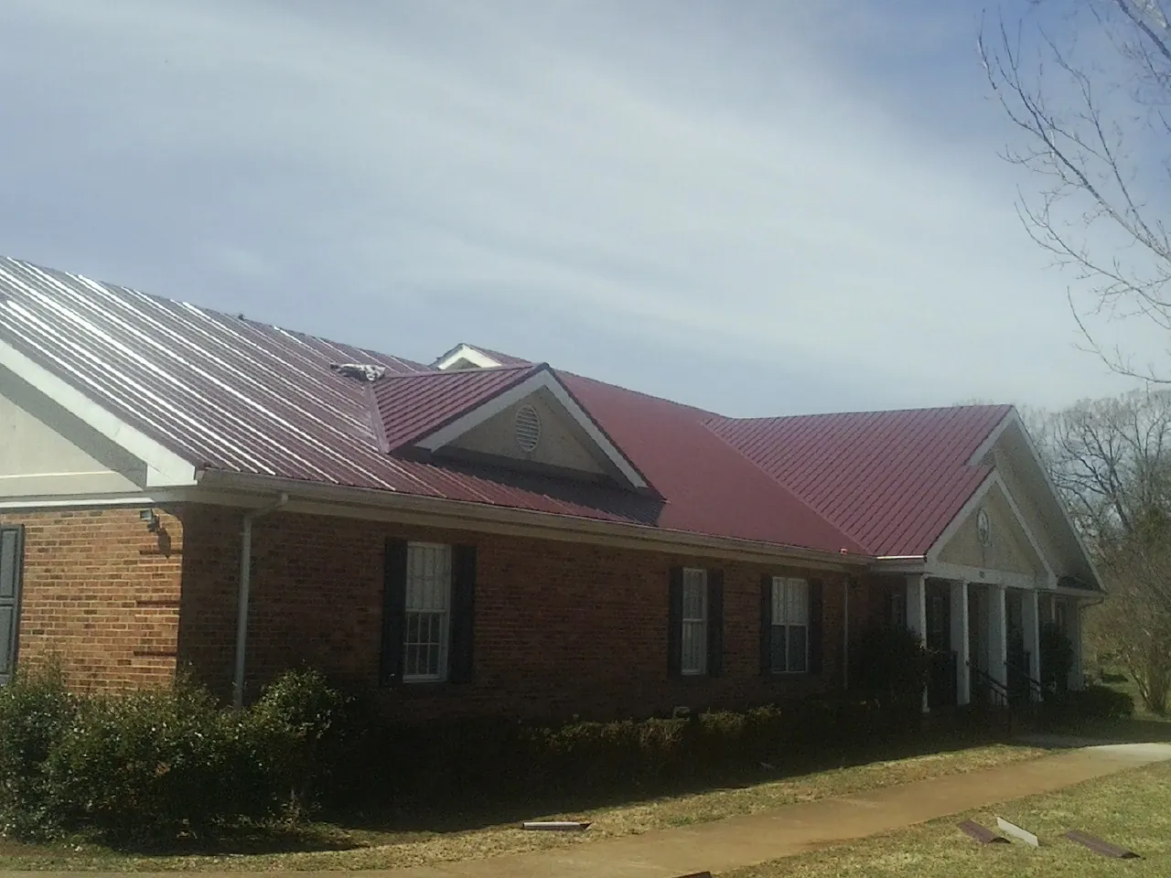 Red metal roof with gabled entries on a long brick building, from a Hail Damage Roof Repair job in Farmersville