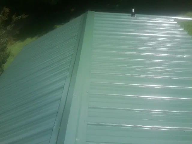New green metal panels meeting at the ridge of a roof — Flat Roof Repair work by our crew in Farmersville