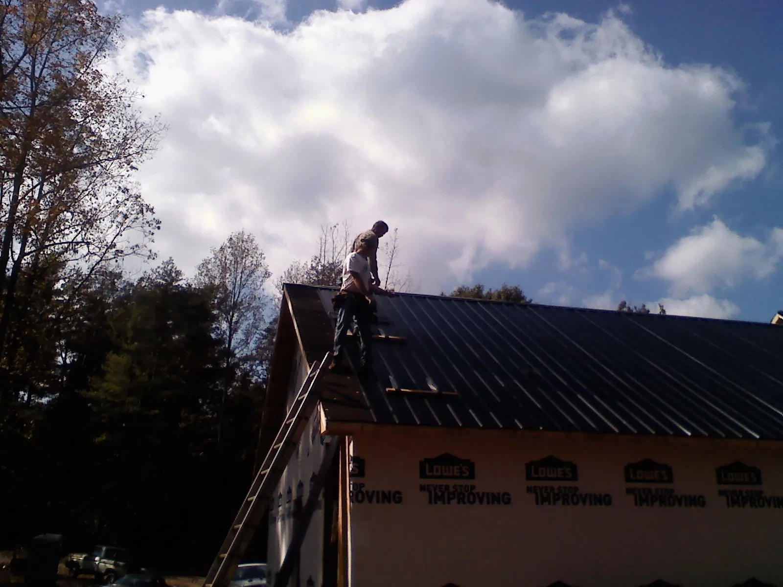 Roofer fastening dark metal panels high against a cloudy sky, from a Roof Inspection job in Farmersville