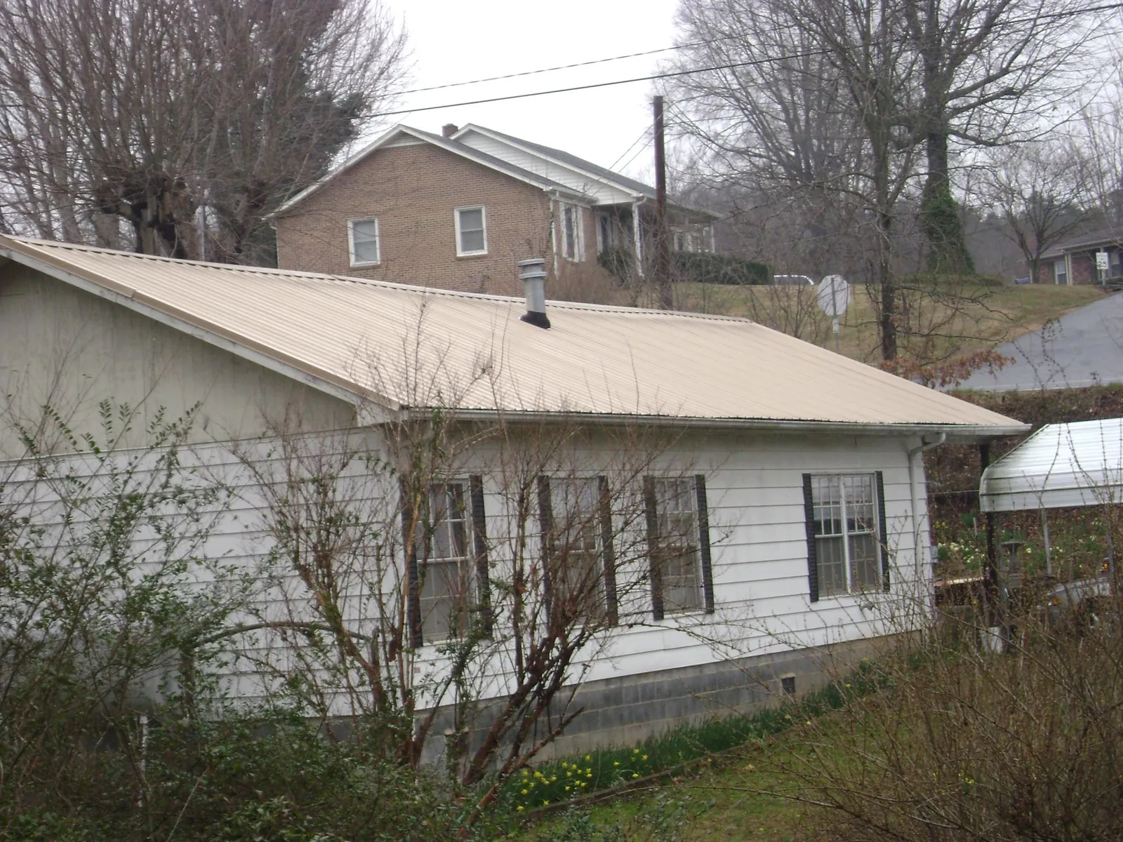 Tan metal roof on a white sided house set into a hillside — Commercial Roofing by Roofing Brothers in Farmersville