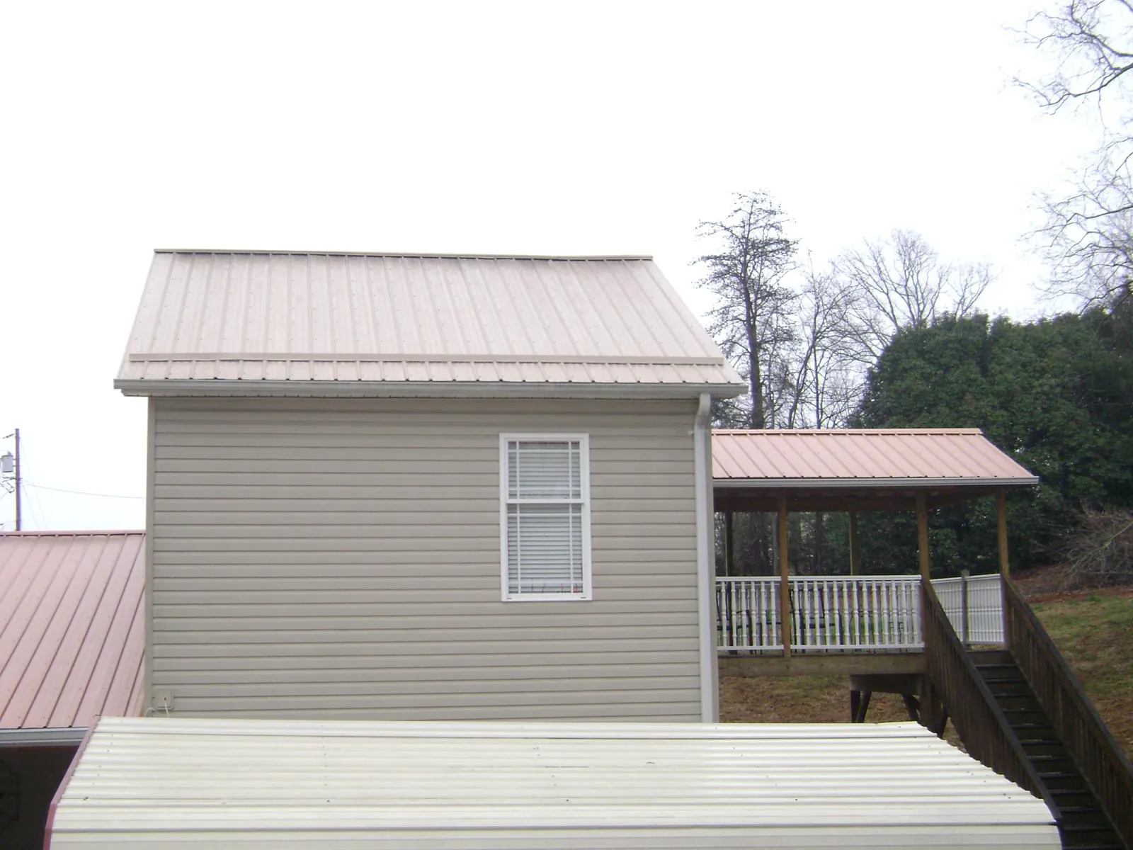 Tan metal roofs on a two story addition and attached porch, from a Roof Replacement job in Farmersville